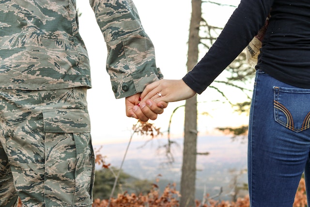 Image shows a male caucasian soldier's hand holding a female caucasian partner's hand that has an engagement ring on it.