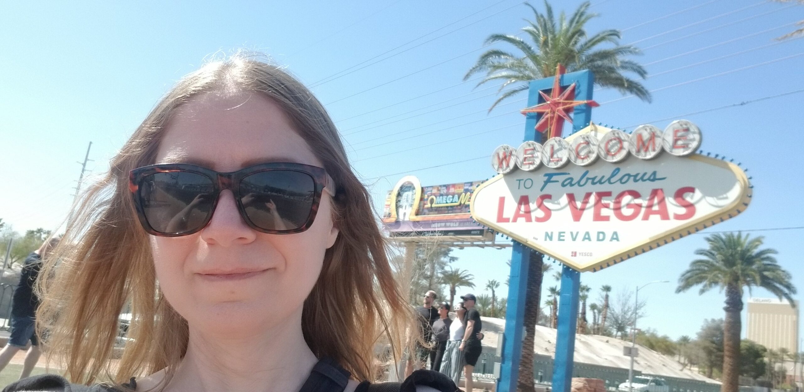 Image shows the author, an early forties caucasian female with medium length blonde hair, outside on a sunny day wearing sunglasses. The Las Vegas sign is behind her to the right.