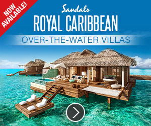 Image is a photo of an over-the-water villa at the Sandals Royal Caribbean resort in Jamaica on a sunny day. The villa has a thatched roof a large deck, and some steps going down to a smaller deck with lounge chairs right on the turquoise water.